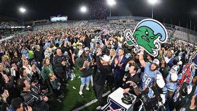 Fans celebrate on a football field at night, confetti falling, person holding a Tulane Angry Wave logo.