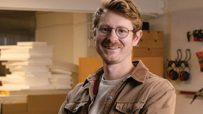 Smiling man with glasses and mustache in a workshop.