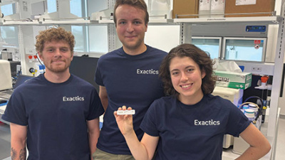 Three smiling team members in a lab, one person holds an Exactics test.