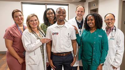 Seven smiling medical staff members and a young man in a white polo shirt.