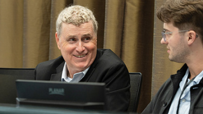 Smiling man with blond hair engages with another man in a meeting.