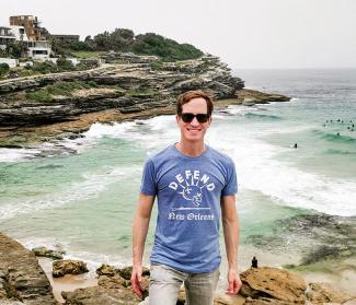 Zachary St. Martin stands in front of ocean wearing a "Defend New Orleans" T-shirt