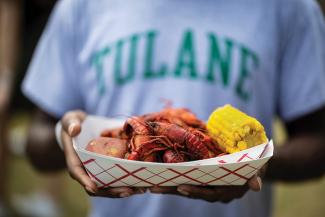 Hands holding a plate of boiled crawfish, corn and potato.