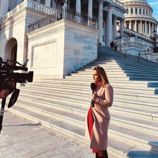 Ali Vitali stands in front of Capitol Hill and reports in front of a TV camera.
