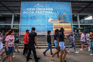 people walk outside past a banner for New Orleans Book Festival on Tulane campus