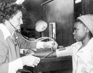 old black and white photo of nurse measuring a child's blood pressure