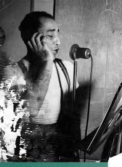 old black and white photo of Louis Prima singing into a microphone in a recording booth