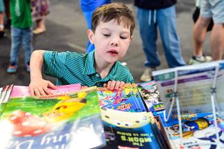 young boy stretches to look at a table filled with books.