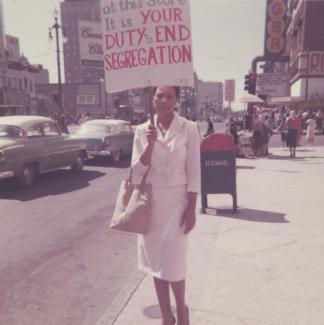 Doris Jean Castle holds a sign reading "it is your duty to end segregation" while standing on city sidewalk