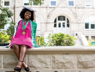 graduate Alexa Authorlee sits on the Tulane stone sign in front of Gibson Hall