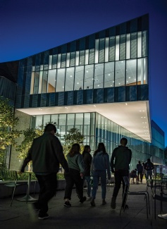 A dusk scene of students walking in front of a glass building