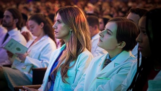 medical students wearing white coats are seated in an audience