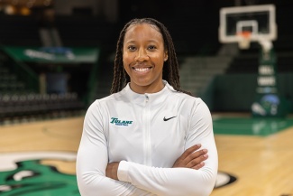 Ashley Langford smiles and poses with arms folded on a basketball court