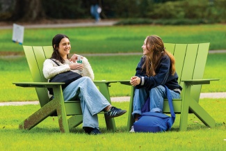 two students conversing outside in green chairs on a green lawn