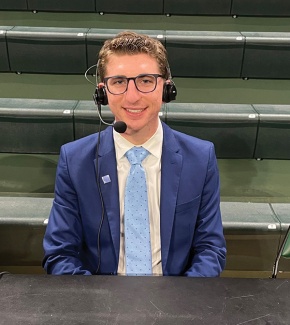 Isaac Popper wears broadcast headset while on the sidelines of a sports court