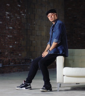 Bobby Yan wears a blue shirt and leans on a white armchair