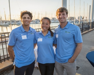 Three Tulane Sailing team members pose by a marina at sunset