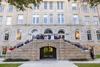 A group of students stand on the exterior stone staircase of historic Richardson Memorial Hall