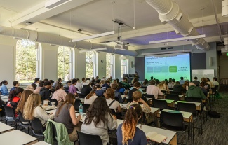students in lecture hall with large windows and a large screen display