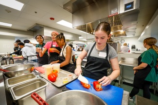 A group of students learning to cut peppers in a kitchen