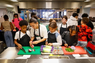 A group of young students in a kitchen learning to cut vegetables