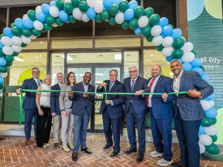 Tulane leaders and community members stand under blue and green balloons and cut a grand opening ribbon 