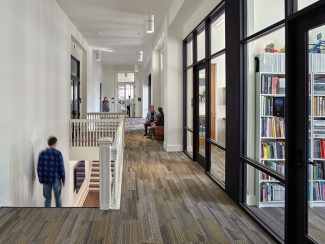 A student descends the stairs in Richardson Memorial Hall. A library room is visible behind glass walls.