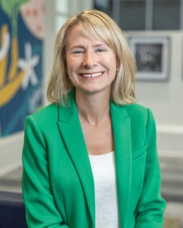 A portrait of Amelia Manning wearing a bright green blazer, photographed in an office setting. 