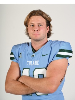 Football player in a light blue Tulane jersey, arms crossed, looking confident. White background, short brown hair, calm expression.