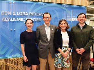 The Peters family: duaghter, father (Don), mother (Lora) and son stand in front of a blue sign that reads "Don & Lora Peters Academic Center".