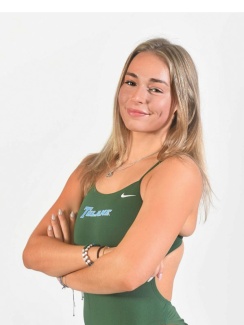 Young woman in a green athletic swinsuit with crossed arms, smiling confidently.