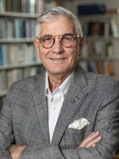 Portrait of Randy Sparks smiling, wearing a gray plaid suit and white shirt, stands in a library with crossed arms; conveys confidence and warmth.