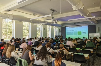 Students attend a lecture seated in rows of desk in a newly remodeled classroom. Slides are projected on a large screen.A large screen 
