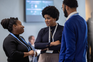 Three people engaged in conversation at a conference. They are wearing lanyards and appear focused and engaged.
