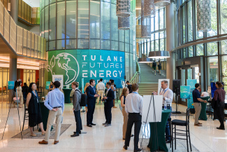People socialize in a modern, spacious atrium at the Tulane Future Energy conference. Large windows create a lively atmosphere.