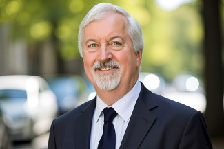 Bill Templeton in a suit smiling outdoors, with blurred trees and cars in the background. The scene conveys a professional and approachable tone.