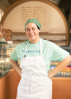 Smiling baker in a green bandana and apron in a bright bakery.