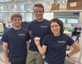 Three smiling team members in a lab, one person holds an Exactics test.