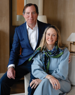 Smiling man in blue suit and woman in light blue outfit with patterned scarf.