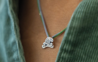 Silver wave pendant necklace with a colorful cord against a green shirt.