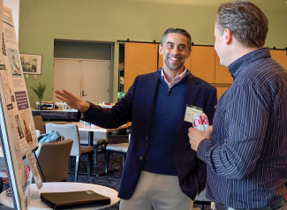 Two men conversing at a conference, one smiling and pointing at a presentation poster.