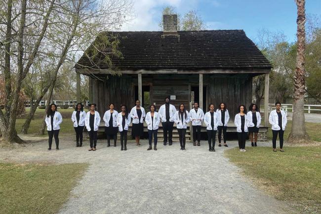 15 Black medical school students in white coatspose in front of Whitney Plantaion
