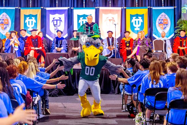 Riptide (pelican mascot) high fives the student crowd at Convocation 