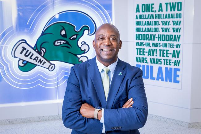 David Harris, wearing a blue suit, poses in front of Angry Wave and a Tulane cheer sign.