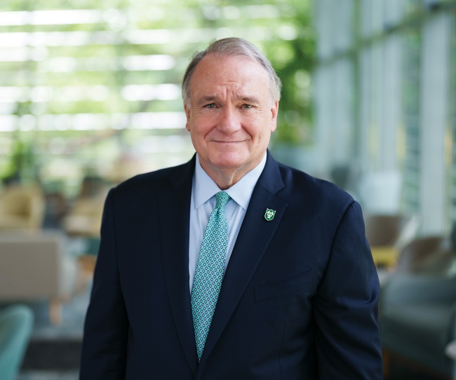 President Fitts portrait in a building lobby with greenery visible through large windows