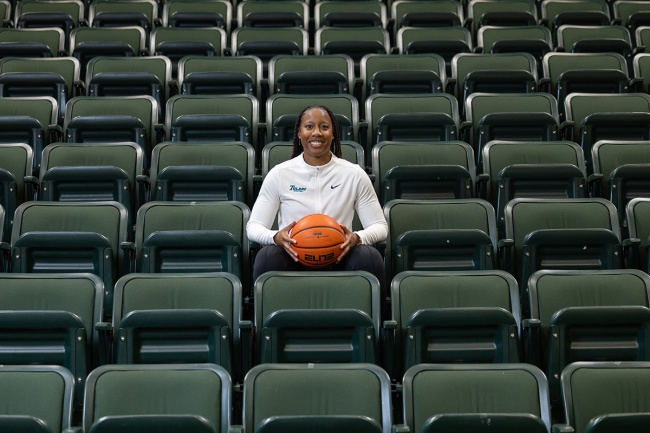 Ashley Langford sits among empty green arena seats and holds a basketball