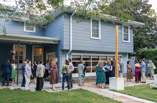 Guests gather outside at the a blue residential house for the dedication ceremony