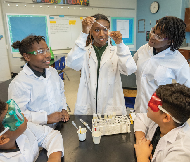 Students in lab coats doing a science experiment with pipettes and test tubes.