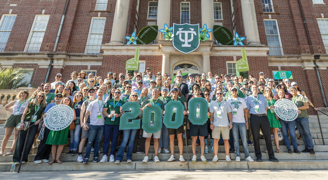 Alumni gathering on steps of brick building, holding large green "2000" numbers.